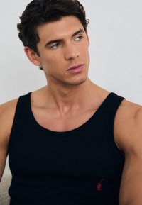 Schwarzes geripptes Tank-Top aus einem weichen Material mit einem kleinen roten Logo an der Seite, figurbetontes Design, das den Oberkörper hervorhebt.