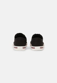Schwarze Segeltuch-Sneaker mit weißen Gummisohlen, die rote und blaue gestreifte Akzente sowie ein Logo auf der Ferse haben. Abgerundete Zehenpartie und niedriges Design.