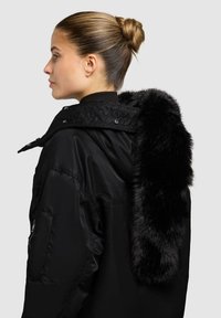 Giacca nera imbottita con design trapuntato e trattamento in pelliccia sintetica sul cappuccio, che presenta una texture liscia e una silhouette elegante.