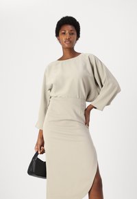 Completo beige a due pezzi composto da una maglietta svasata con scollatura ampia e maniche lunghe, e una gonna a tubino aderente con uno spacco laterale.