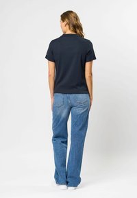 Marineblå ribbestrikket polo med krage, kombinert med lys blå vide bukser og hvite sneakers. Minimalistisk design, uten bemerkelsesverdige mønstre.