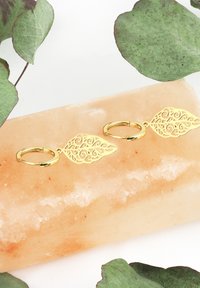 Gul metallnyckelring med intrikata bladformade dekorationer med svängar, som vilar på en rosa saltblock, omgiven av gröna blad.