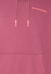 Sweat à capuche rose poudré avec poche avant, cordons assortis et petit logo "Scotch & Soda" en rose clair sur la poitrine.