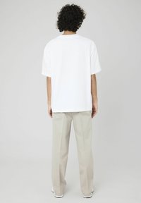 T-shirt en coton blanc à manches courtes avec un ourlet droit, associé à un pantalon beige clair bien ajusté et des baskets blanches, vu de dos.