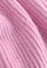 Lyserødt strikket stof med en ribbet tekstur, der har bløde, fuzzy fibre og varierende nuancer af lyserødt over hele overfladen.