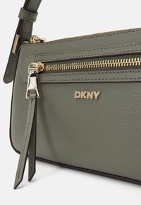 Borsa a spalla verde in pelle con superficie testurizzata, hardware dorato e una zip prominente. Presenta il logo DKNY e una tracolla removibile.