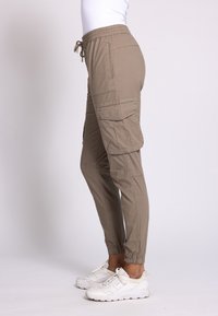 Beige Cargohosen mit Seitentaschen, elastischem Bund und gekrempelten Bündchen, aus leichtem Stoff, kombiniert mit weißen Sneakern.