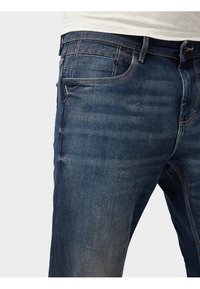 Vaqueros de mezclilla azul oscuro con un corte clásico. Cuenta con cinco bolsillos, costuras visibles y una ligera textura desgastada a lo largo de los muslos.