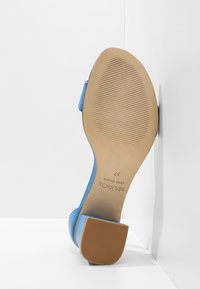 Sandale à talon haut bleue avec une tige en cuir lisse et une semelle en caoutchouc beige. Dispose d'un talon proéminent et d'une surface inférieure texturée pour une meilleure adhérence.