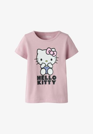 Różowy t-shirt z krótkim rękawem z postacią Hello Kitty w niebieskich ogrodniczkach i różową kokardką, z napisem „HELLO KITTY” pod grafiką.