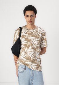Brun kortærmet t-shirt med hvidt bladmønster, parret med lyseblå jeans og en sort skuldertaske med en lynlåslomme.