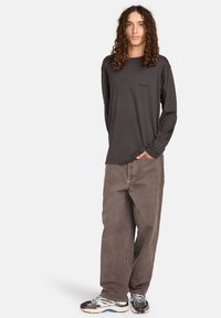 Langärmliges graues Shirt mit einem runden Ausschnitt, kombiniert mit lockeren braunen Hosen und mehrfarbigen Sportschuhen.