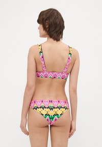 Multifarvet bikini med et geometrisk mønster i pink, gul og grøn. Tykk strop på toppen og et lavt skåret bunddesign.
