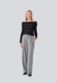 Top nero con spalline scoperte e maniche lunghe, abbinato a pantaloni grigi a vita alta con pieghe e silhouette a gamba larga.