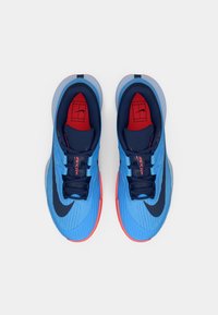 Siniset urheilukengät, joissa on teksturoitu päällinen, laivastonsinisiä yksityiskohtia, punaiset sisäpohjat ja selkeä musta swoosh-logo sivussa.