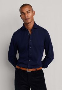 Marineblauw overhemd met knopen, slim fit, lange mouwen, een gespreide kraag en lichtblauwe knopen, gecombineerd met donkere broek en een leren riem in bruin.