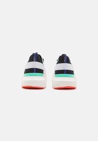 Footwear featuring a black and white upper, green accents, a thick white midsole, and a bright orange outsole. Branding visible on the heel.