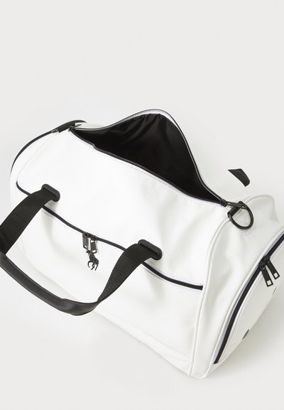 Vit duffelväska i syntetmaterial, med svarta accenter, två svarta handtag och dragkedjestängning med en svart innerfoder.