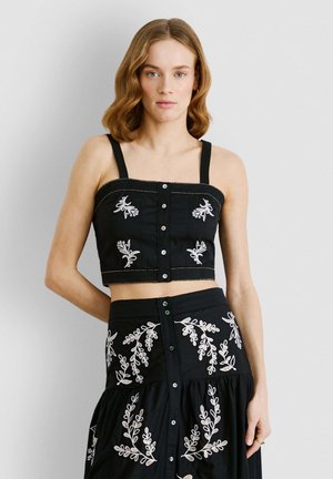 Top corto nero con spalline spesse, chiusura con bottoni e dettagli in ricamo floreale bianco. Tessuto liscio con un design aderente.