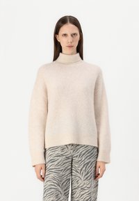 Hellbeige, Turtleneck-Pullover aus weichem, strukturiertem Stoff mit lockerer Passform, kombiniert mit grauen Hosen im Zebra-Print mit weitem Bein.