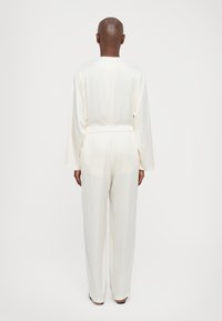 Mono blanco ligero con mangas largas y cinturilla elástica. Presenta un diseño de pierna recta y una textura suave.