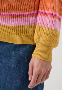 Knitted sweater with multicolored stripes in orange, pink, and yellow. The cuff is ribbed, and the fabric appears textured and cozy.