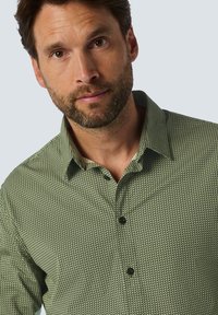 Hemd aus texturiertem grünem Stoff mit geometrischem Muster, versehen mit einem spitzen Kragen und schwarzen Knöpfen an der Vorderseite.