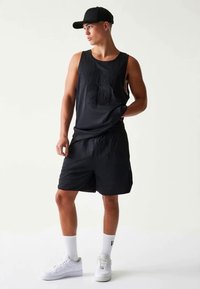 Black athletic tank top with embossed "20" design, paired with matching shorts. Worn with white sneakers and ankle socks, under a black cap.