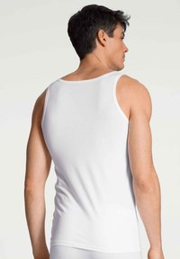 Débardeur blanc en tissu lisse, présentant une coupe classique avec de larges emmanchures et un col rond, vu de dos.