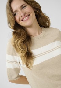 Suéter de punto beige con mangas cortas, con rayas horizontales blancas y un cuello acanalado. Textura suave, corte relajado.