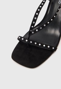 Sandal din suede negru cu vârf pătrat plat, având două curele subțiri decorate cu strasuri clare pentru un plus de detaliu. Textură moale.