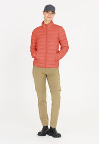 Vadderad koralljacka med hög krage och dragkedja; tillsammans med ljus khaki cargobyxor och svarta ankelstövlar. Enkelt design, inga synliga mönster.