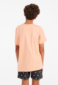 Perzikkleurig katoenen T-shirt met korte mouwen, gedragen met zwarte shorts met een kleine palmbomenprint. Eenvoudig ontwerp en comfortabele pasvorm.
