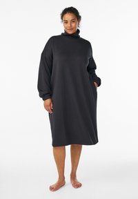 Svart sweatshirtklänning med hög krage, sänkta axlar, långa ärmar, sidofickor och en lös, avslappnad passform. Mjuk tygtextur.