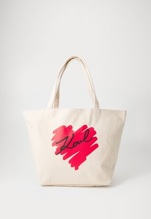 Bolso de lona beige con asas dobles, con un corazón pintado con pincel en rojo y la palabra manuscrita en negro "Karl" en el frente.