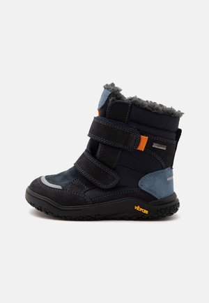 Botte d'hiver enfant noire et marine avec deux bandes Velcro, doublure polaire, patch bleu au talon et semelle Vibram sur fond blanc.