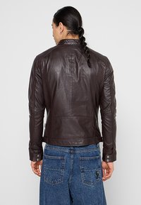 Hnědá kožená bunda s přizpůsobeným střihem, hladkou texturou a jemnými švy. Obsahuje akcenty se snap tlačítky a design s kulatým límcem.