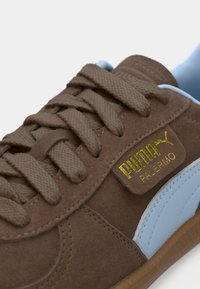 Pruunist nahkainetisest tossust koosneb helesiniste detailidega, tekstuursete paelte ja kuldse logotagiga, millel on kiri "PUMA PALERMO", külgpinnal.