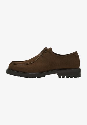 Chaussure en suede marron avec un bout arrondi, des coutures contrastantes, des lacets plats, et une semelle en caoutchouc noir texturé pour une meilleure traction et durabilité.