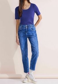 Lila kortärmad topp i kombination med ljusblå avslappnade jeans och vita sneakers. Jeansen har knappstängning och framfickor.