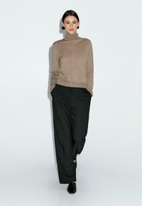 Beżowy sweter z golfem zestawiony z luźnymi czarnymi spodniami. Sweter ma dopasowany pas i teksturowany materiał; spodnie są plisowane i mają swobodny krój.