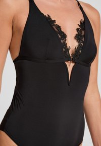 Zwarte bikini met een diepe V-halslijn, voorzien van ingewikkelde zwarte kantdetails op de buste en een klein sleufaccent in het midden.