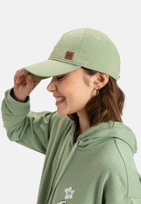 Green baseball cap made of cotton twill, featuring white stitching and a brown brand patch. Worn with a matching green hooded sweatshirt.