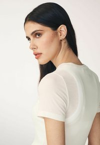 Weißes geripptes T-Shirt mit kurzen Ärmeln, das eine glatte Textur und eine taillierte Silhouette aufweist. Auffälliger Rundhalsausschnitt und minimale Markenkennzeichnung auf der Rückseite.