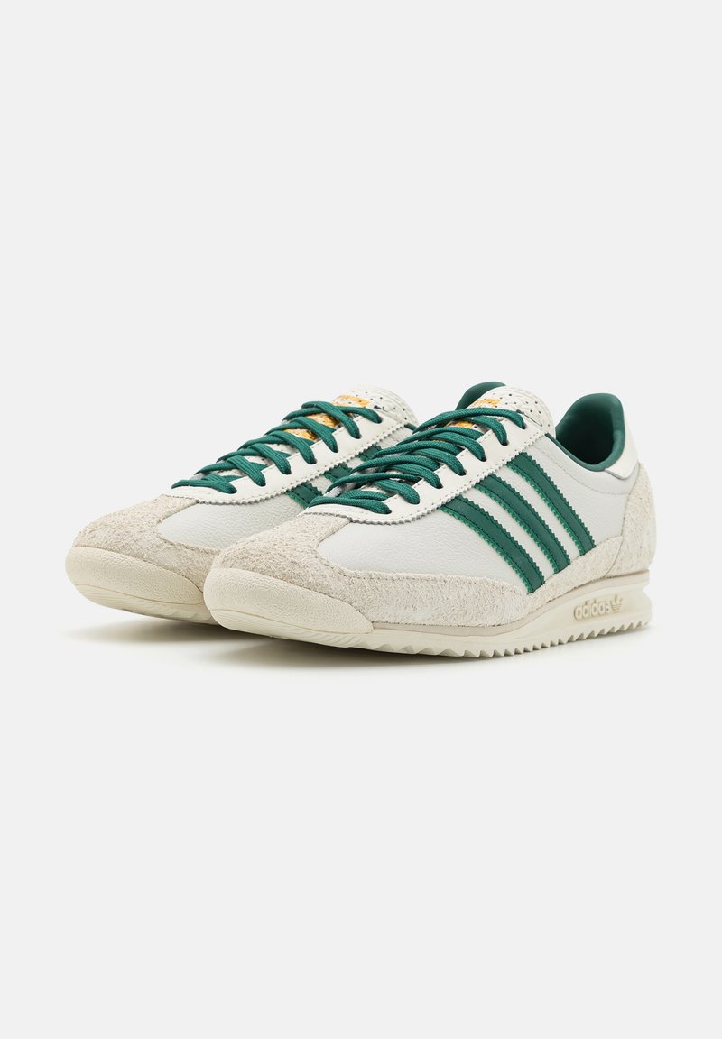 Baskets blanches de sport avec des accents verts, en matières suède et cuir, design à trois bandes, semelle en caoutchouc texturée de couleur crème.