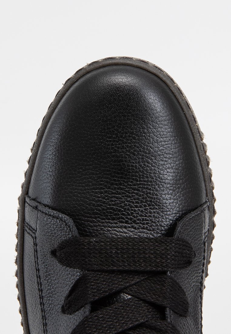 Sneakers en cuir noir avec une surface texturée, bout rond et lacets foncés. Semelle en caoutchouc notable avec un bord à motifs.