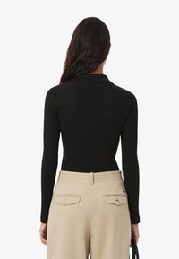 Svart ribbad topp med lång ärm och krage, matchad med beige byxor som har två bakfickor och en synlig logotyp.