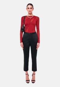 Röd långärmad bodysuit med genomskinliga sektioner, parat med skräddarsydda svarta byxor och svarta remsandaler. Liten svart handväska och pärlkrage.