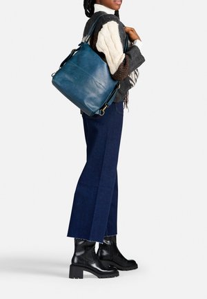 Blauwe leren handtas met een gestructureerde vorm, verstelbare schouderriem en gouden hardware, gecombineerd met donkere wijde jeans en zwarte chunky laarzen.