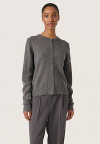 Cardigan gri tricotat cu guler rotund, nasturi frontali și mansete cu model în relief. Purtați peste pantaloni gri cu dungi, evidențiind o textură moale.